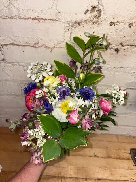 Bouquet of colorful flowers held against a rustic brick wall.